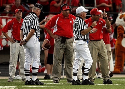 Football officials on sidelines with coaches.